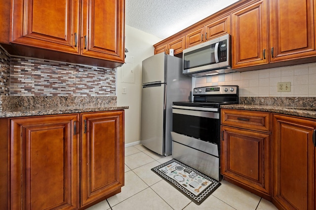 kitchen with dark stone counters, a textured ceiling, decorative backsplash, light tile patterned floors, and appliances with stainless steel finishes