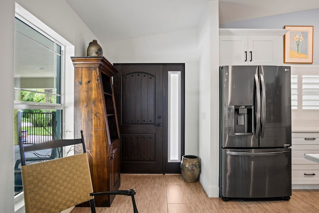 kitchen featuring light hardwood / wood-style flooring, stainless steel fridge, vaulted ceiling, and white cabinetry