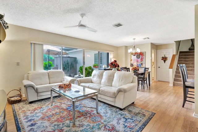 living room featuring ceiling fan with notable chandelier, light hardwood / wood-style floors, and a textured ceiling