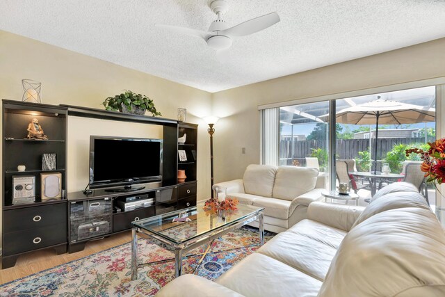 living room featuring light wood-type flooring, ceiling fan, and a textured ceiling