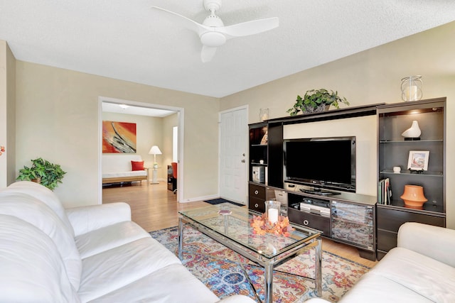 living room featuring light wood-type flooring, ceiling fan, and a textured ceiling