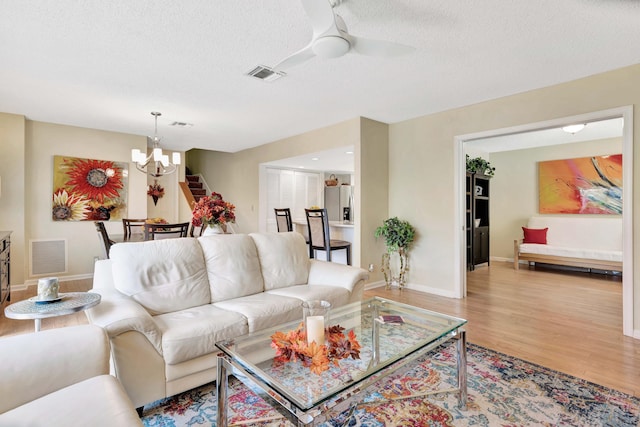 living room featuring ceiling fan with notable chandelier, a textured ceiling, and hardwood / wood-style floors