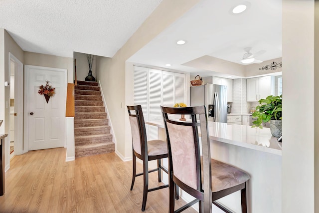 kitchen featuring white cabinets, stainless steel refrigerator with ice dispenser, light wood-type flooring, and a kitchen breakfast bar