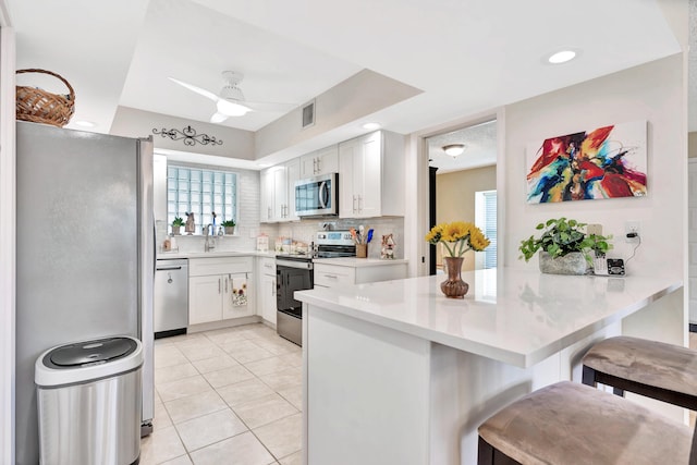 kitchen featuring white cabinets, kitchen peninsula, a breakfast bar area, stainless steel appliances, and ceiling fan