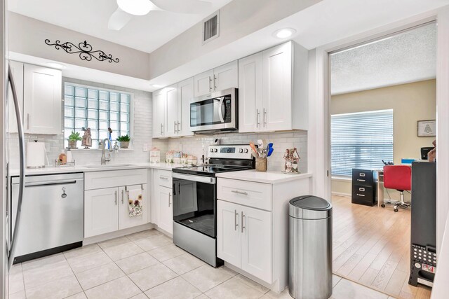 kitchen with sink, white cabinetry, stainless steel appliances, light hardwood / wood-style floors, and decorative backsplash