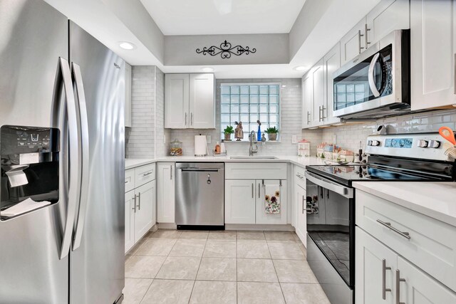 kitchen with white cabinets, light tile patterned flooring, sink, appliances with stainless steel finishes, and decorative backsplash