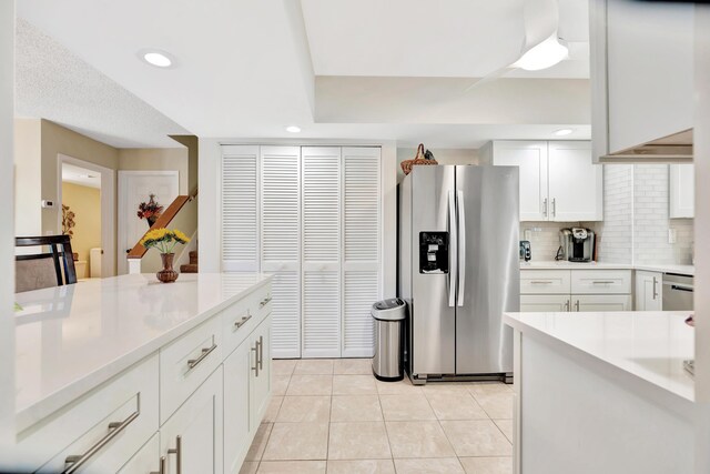 kitchen with stainless steel refrigerator with ice dispenser, white cabinetry, decorative backsplash, and light tile patterned floors