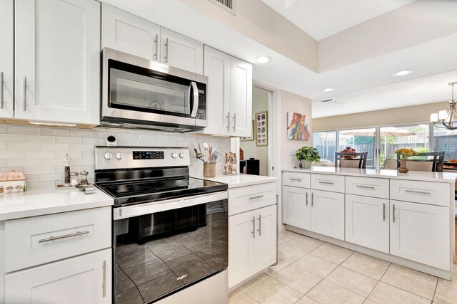 kitchen featuring a chandelier, white cabinetry, decorative backsplash, appliances with stainless steel finishes, and light tile patterned floors