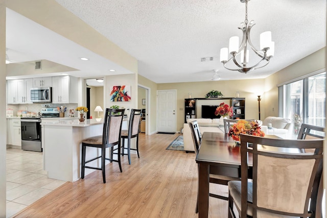 dining space with ceiling fan with notable chandelier, light hardwood / wood-style floors, and a textured ceiling