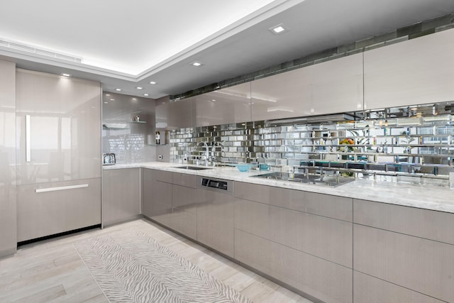 kitchen featuring light stone countertops, tasteful backsplash, gas stovetop, sink, and light hardwood / wood-style floors