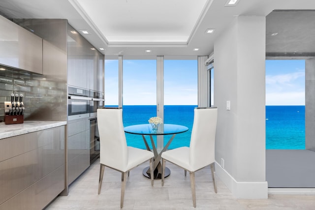 dining area with a tray ceiling, a water view, and light hardwood / wood-style floors