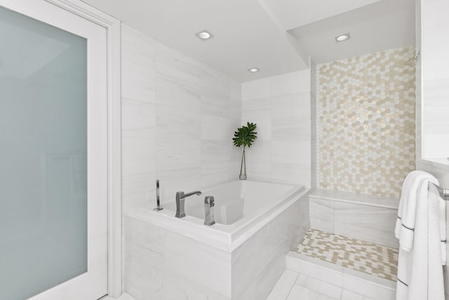 bathroom with tile patterned flooring, a relaxing tiled tub, and tile walls