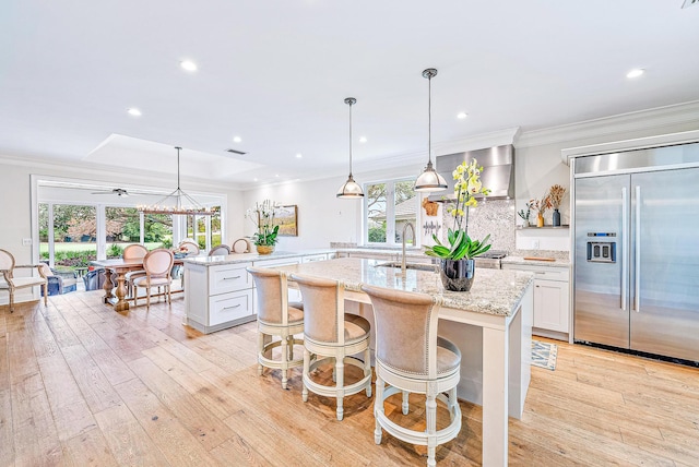 kitchen with stainless steel built in fridge, white cabinetry, plenty of natural light, and a kitchen island with sink