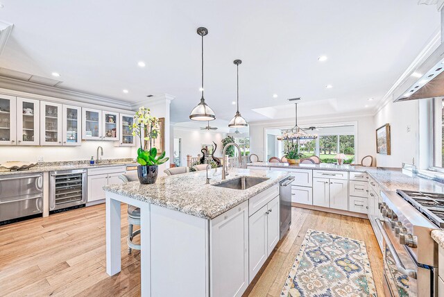 18587 SE Ferland Ct, Jupiter, FL 33469 - kitchen with light wood-style flooring, ornamental molding, appliances with stainless steel finishes, a sink, and beverage cooler