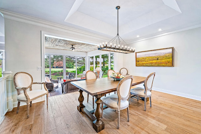 dining area featuring light wood-type flooring, ceiling fan with notable chandelier, and a tray ceiling