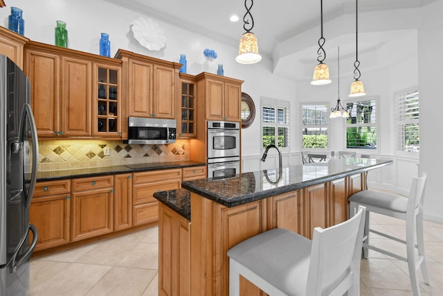 kitchen featuring dark stone counters, a breakfast bar, a kitchen island, appliances with stainless steel finishes, and decorative light fixtures