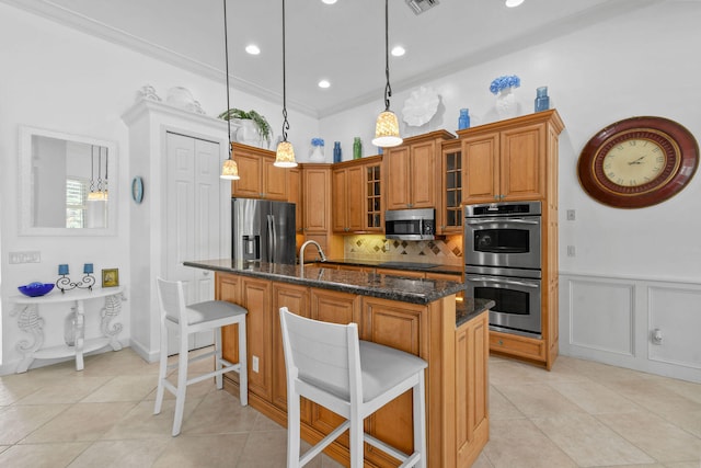 kitchen with dark stone counters, a center island with sink, stainless steel appliances, and a kitchen breakfast bar