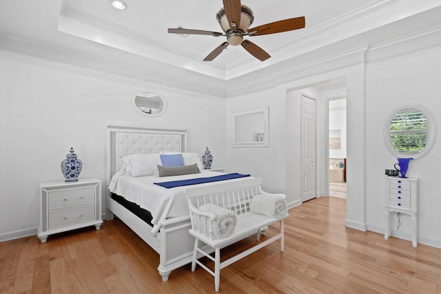bedroom featuring ornamental molding, a ceiling fan, a tray ceiling, and light wood-type flooring