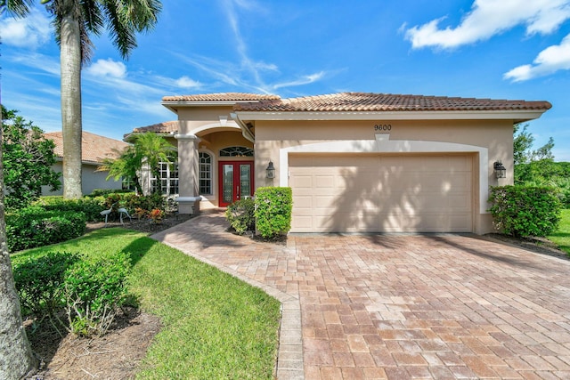 mediterranean / spanish home with french doors, a tile roof, decorative driveway, an attached garage, and stucco siding