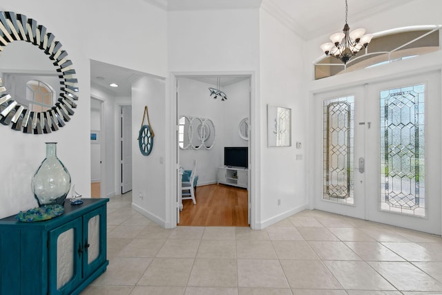 tiled foyer entrance featuring french doors, ornamental molding, a high ceiling, and a notable chandelier