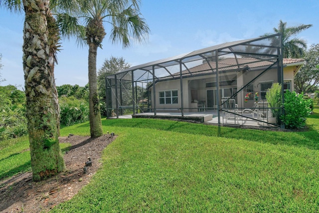 rear view of house featuring a patio, glass enclosure, stucco siding, and a yard