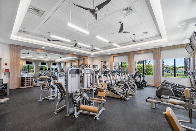 gym featuring ceiling fan, a raised ceiling, and a healthy amount of sunlight