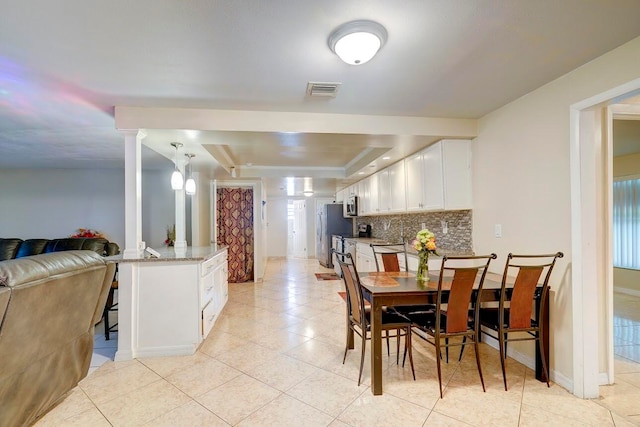 dining space with decorative columns and a tray ceiling