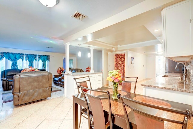 tiled dining area featuring ornate columns, a tray ceiling, and sink