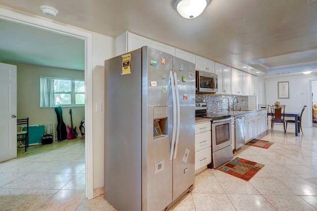 kitchen featuring sink, white cabinets, decorative backsplash, a raised ceiling, and appliances with stainless steel finishes