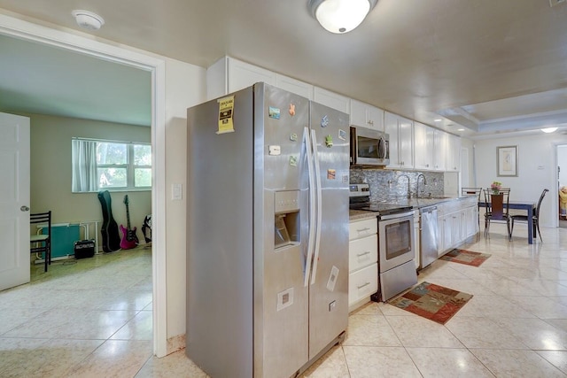 kitchen with a sink, light tile patterned floors, stainless steel appliances, white cabinets, and backsplash
