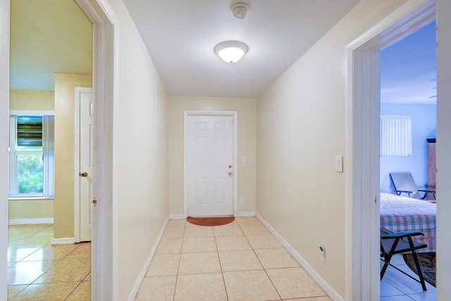 hall with baseboards, light tile patterned flooring, and a healthy amount of sunlight