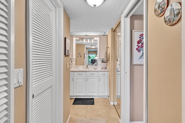 hall with a textured ceiling, light tile patterned floors, and sink