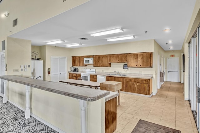 kitchen with white appliances, kitchen peninsula, light tile patterned floors, and sink