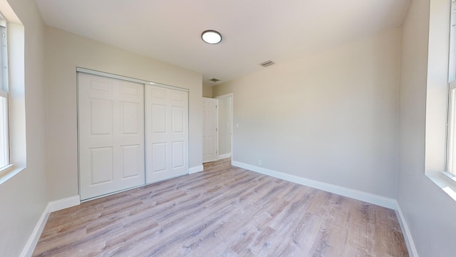 unfurnished bedroom featuring light hardwood / wood-style flooring, a closet, and multiple windows