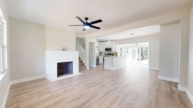 unfurnished living room featuring sink, ceiling fan, light hardwood / wood-style floors, and a brick fireplace