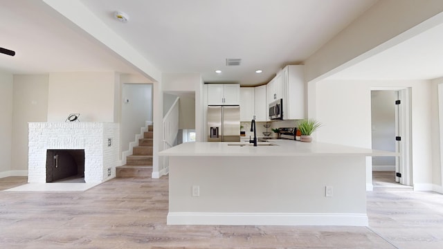 kitchen featuring sink, light hardwood / wood-style flooring, white cabinetry, stainless steel appliances, and a fireplace