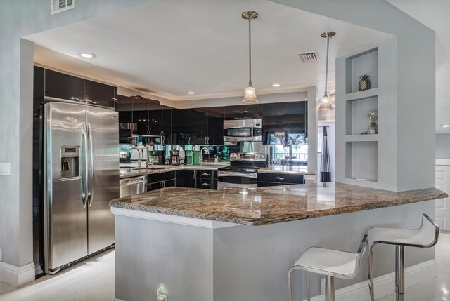 kitchen with light stone counters, pendant lighting, built in features, appliances with stainless steel finishes, and a kitchen bar