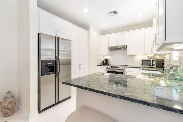 kitchen featuring appliances with stainless steel finishes, decorative backsplash, white cabinetry, kitchen peninsula, and dark stone counters