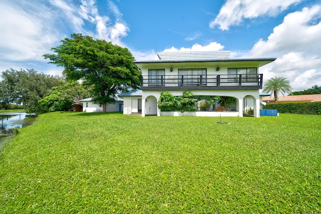 rear view of property with a balcony, a lawn, and a water view