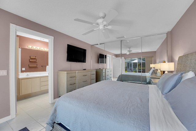 tiled bedroom featuring ceiling fan, connected bathroom, sink, a textured ceiling, and a closet