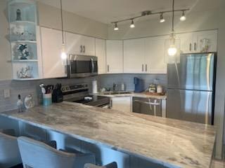 kitchen featuring hanging light fixtures, white cabinetry, stainless steel appliances, light stone countertops, and a kitchen bar