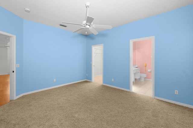 unfurnished bedroom with connected bathroom, a spacious closet, light colored carpet, ceiling fan, and a closet