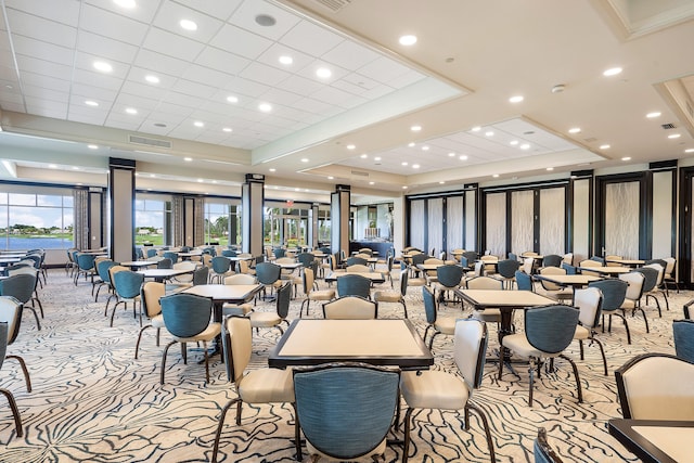 carpeted dining room featuring a raised ceiling and ornate columns