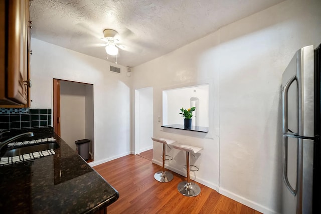 kitchen with a textured ceiling, sink, hardwood / wood-style floors, ceiling fan, and stainless steel fridge