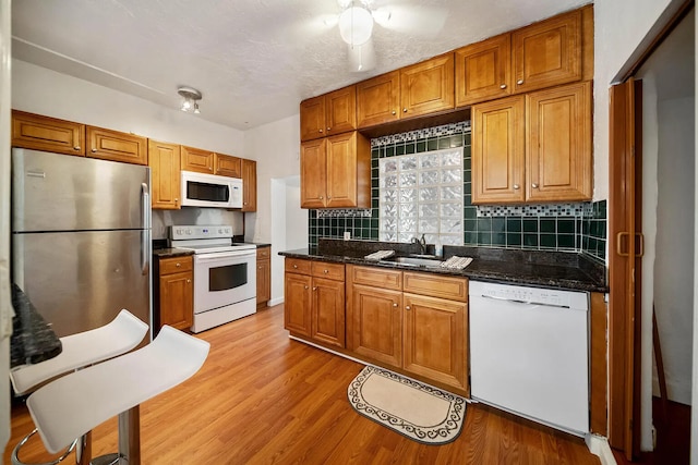 kitchen with dark stone counters, light hardwood / wood-style floors, sink, backsplash, and white appliances