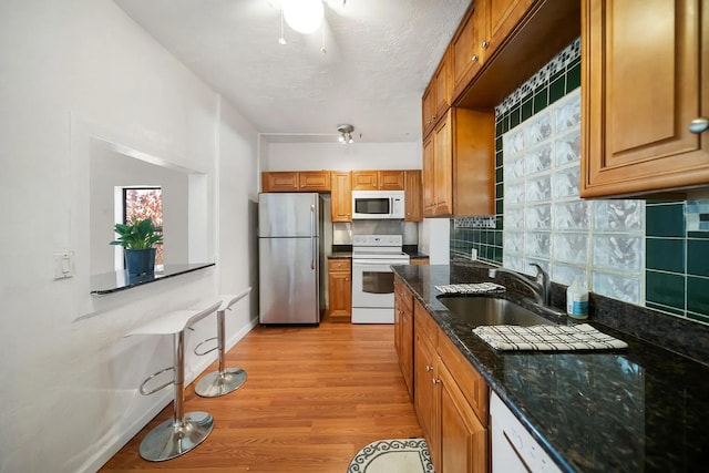 kitchen with light wood-type flooring, sink, backsplash, white appliances, and dark stone countertops