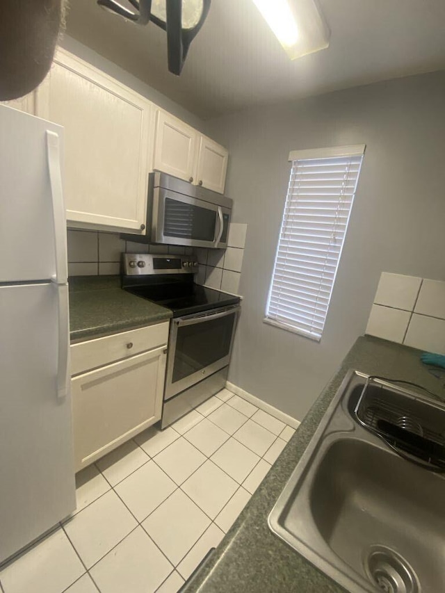 kitchen with appliances with stainless steel finishes, sink, light tile patterned floors, and white cabinets