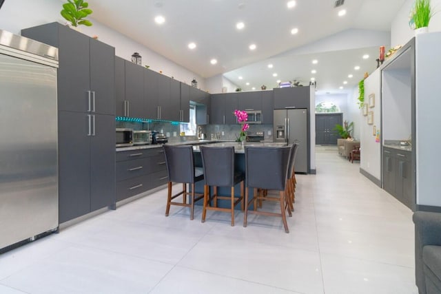 kitchen featuring a breakfast bar area, vaulted ceiling, stainless steel appliances, backsplash, and light tile patterned floors