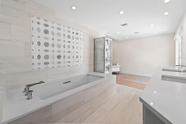 bathroom with hardwood / wood-style floors, vanity, tile walls, and tiled bath