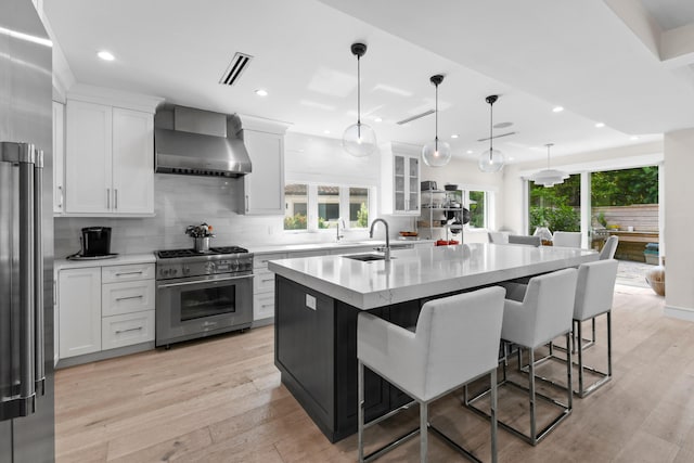 kitchen featuring wall chimney exhaust hood, premium appliances, white cabinetry, and an island with sink